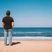 Ambassadeur Tom Frager de dos regardant la plage Oceanides en une journée ensoleillée.